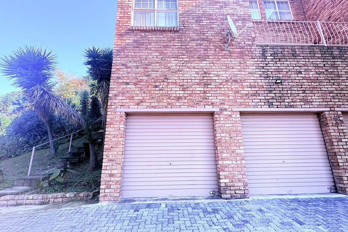 Exterior view of a double garage with face brick facade, paved driveway, and an adjacent external staircase leading to the upper level.