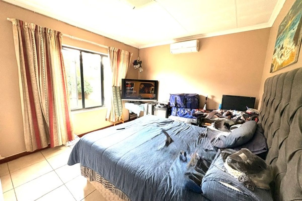 A bedroom featuring tiled flooring and a wall-mounted air conditioning unit, providing a functional space with neutral wall tones.