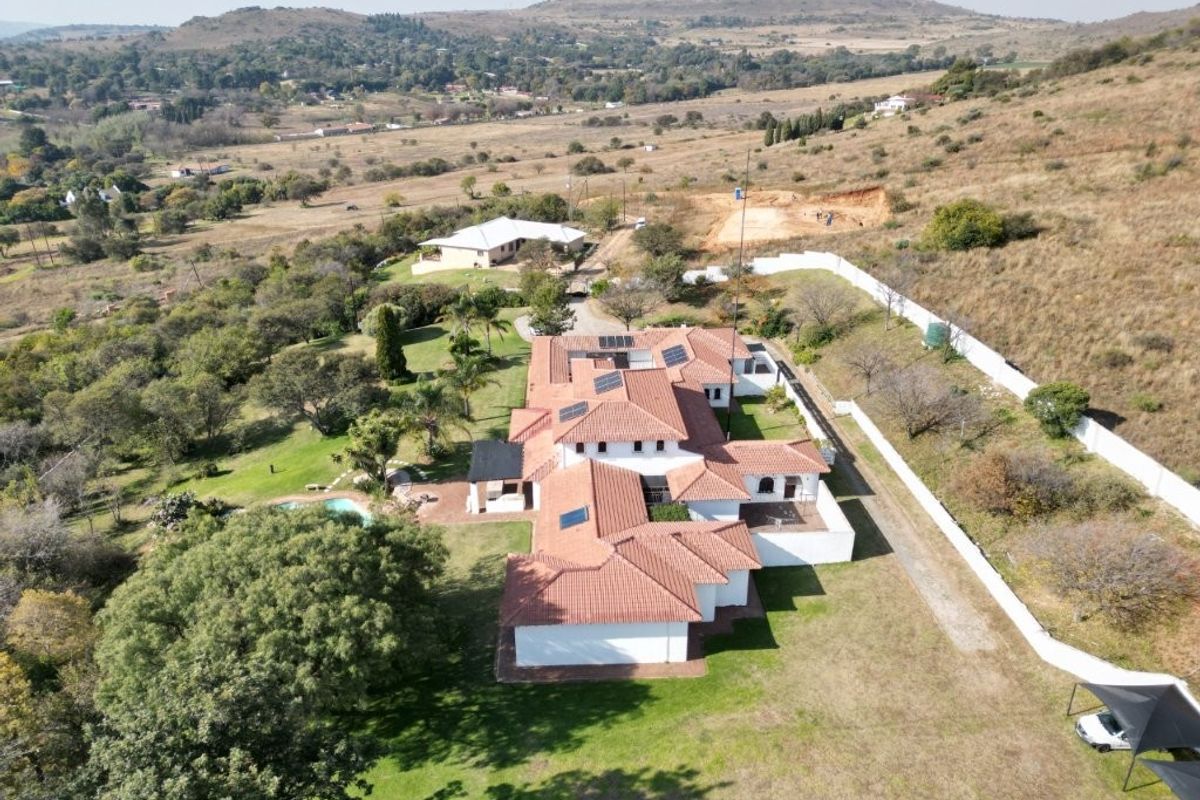 Aerial view of a large residential property featuring a terracotta tile roof with solar panels, a swimming pool, and extensive landscaped grounds.