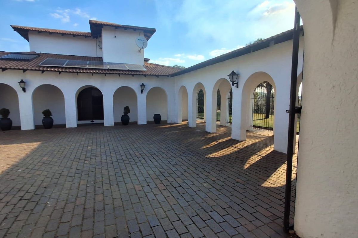 A spacious rear courtyard featuring a classic arched colonnade, brick paving, and integrated solar panels on the roof.