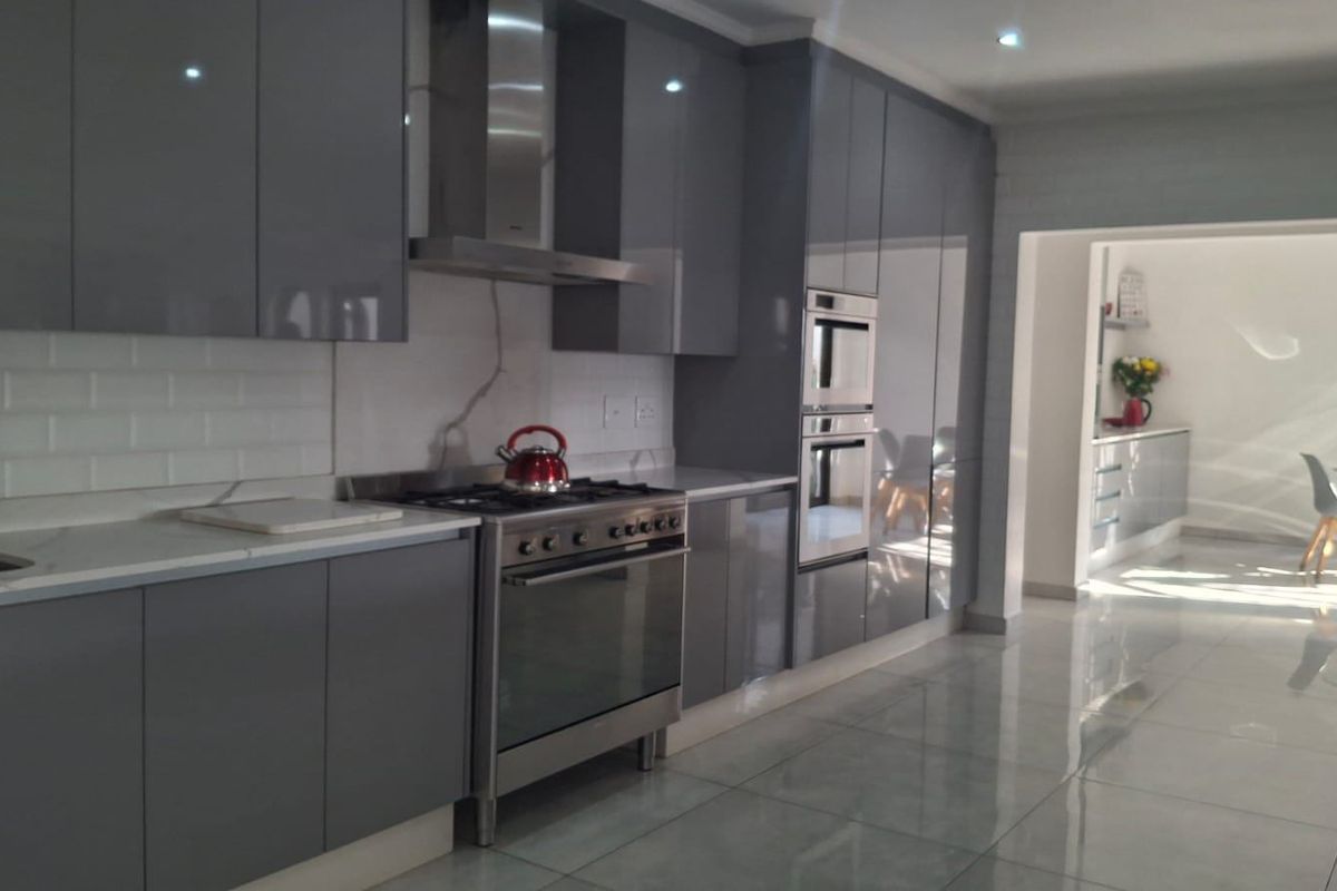 Modern kitchen featuring high-gloss grey cabinetry, stone countertops, subway tile backsplash, and integrated stainless steel appliances, leading into an open-plan dining area.