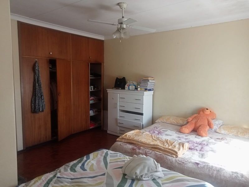 A bedroom featuring built-in wooden cupboards and a ceiling fan, offering a functional space with potential for cosmetic updates.