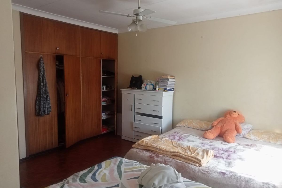 A bedroom featuring built-in wooden cupboards and a ceiling fan, offering a functional space with potential for cosmetic updates.