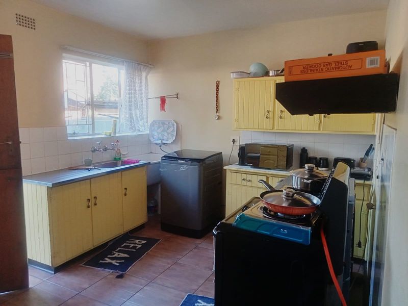 A functional kitchen featuring yellow built-in cabinetry, tiled backsplash, stainless steel sink, and tiled flooring, offering potential for modernization and aesthetic updates.