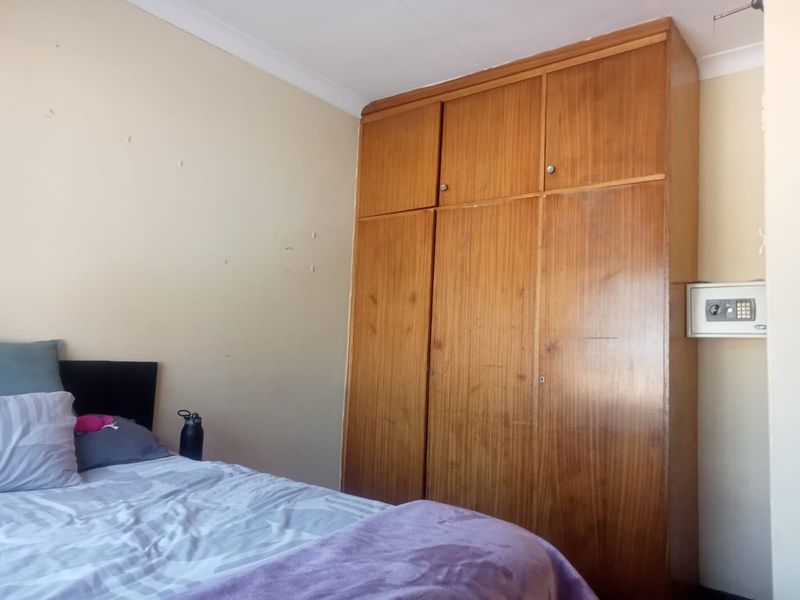 A bedroom featuring a large built-in wooden wardrobe and a wall-mounted safe, offering functional storage space within the room.