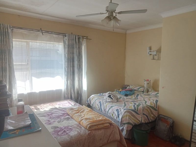 A bedroom featuring a ceiling fan and natural light from a large window, requiring cosmetic updates to the wall finishes.