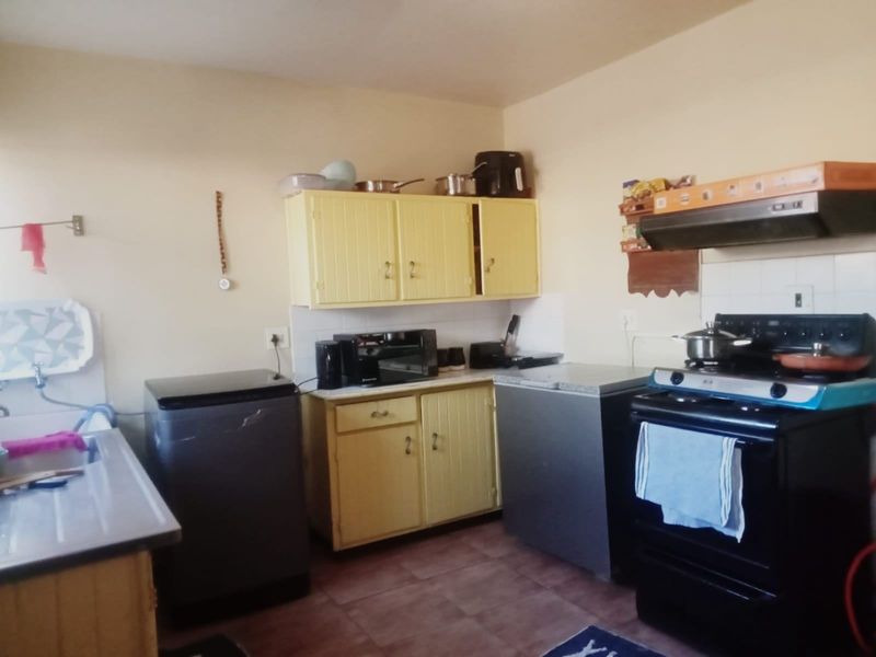 A functional kitchen featuring dated yellow cabinetry, a built-in extractor fan, and tiled flooring, offering potential for a modern renovation.