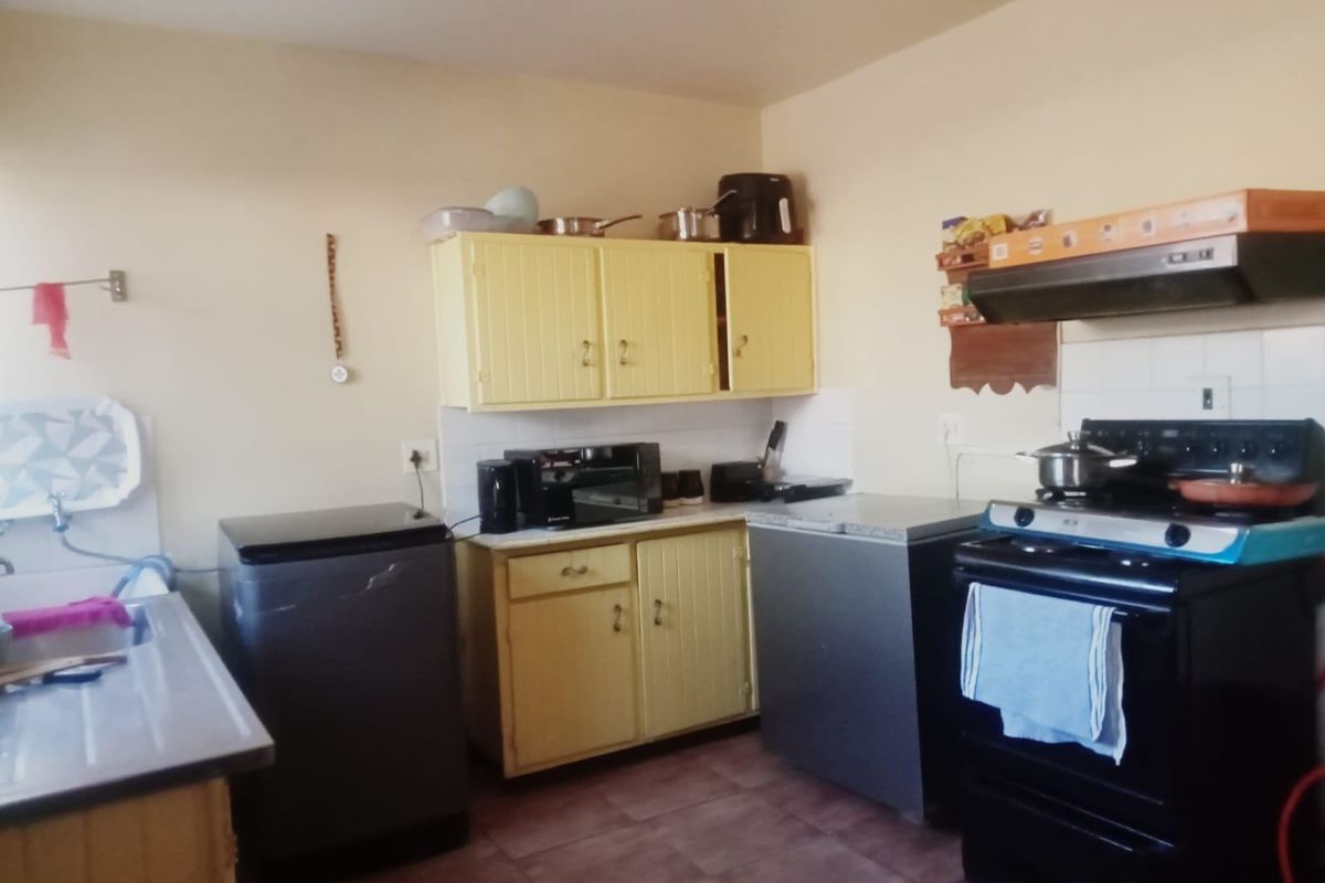 A functional kitchen featuring dated yellow cabinetry, a built-in extractor fan, and tiled flooring, offering potential for a modern renovation.