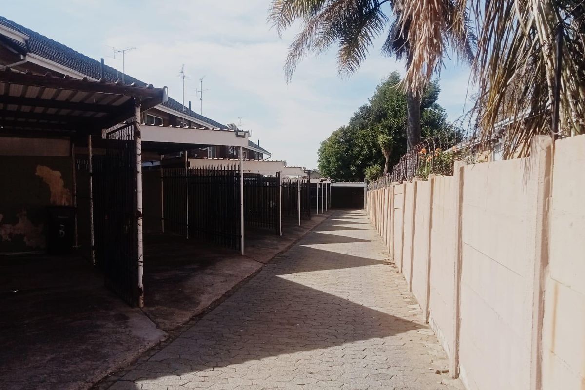 Exterior view of a paved driveway featuring a row of covered carports and a high perimeter boundary wall with security spikes.
