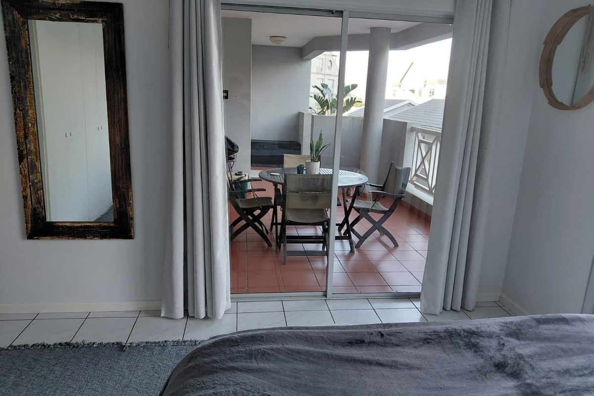A bedroom featuring tiled flooring and sliding glass doors that open onto a covered balcony with outdoor seating.