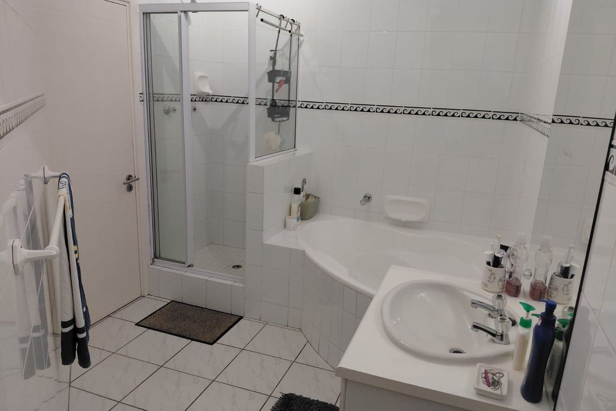 A functional bathroom featuring a tiled shower enclosure, a built-in bathtub, and a vanity basin with white cabinetry.