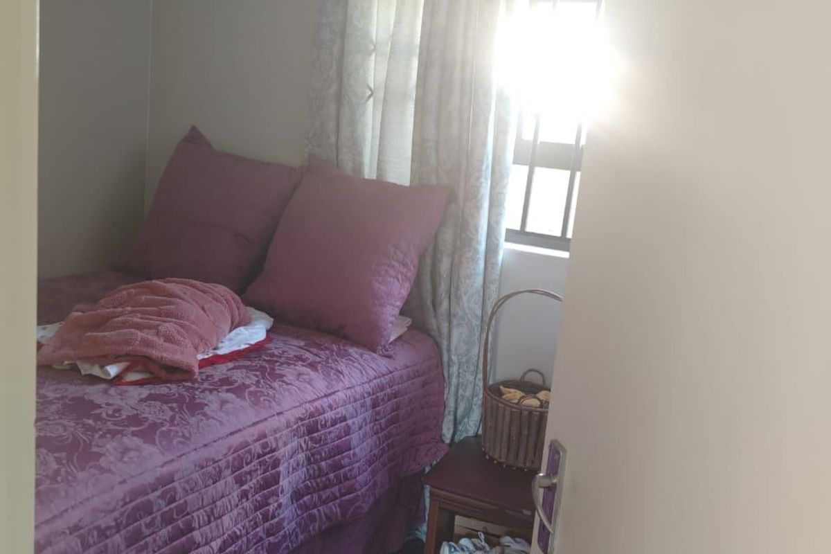 A compact bedroom featuring dark tiled flooring and a window fitted with security bars, viewed from the doorway.