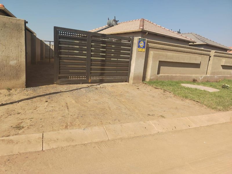 Front view of the property featuring a metal sliding gate, perimeter wall, and solar geyser installed on the tiled roof.