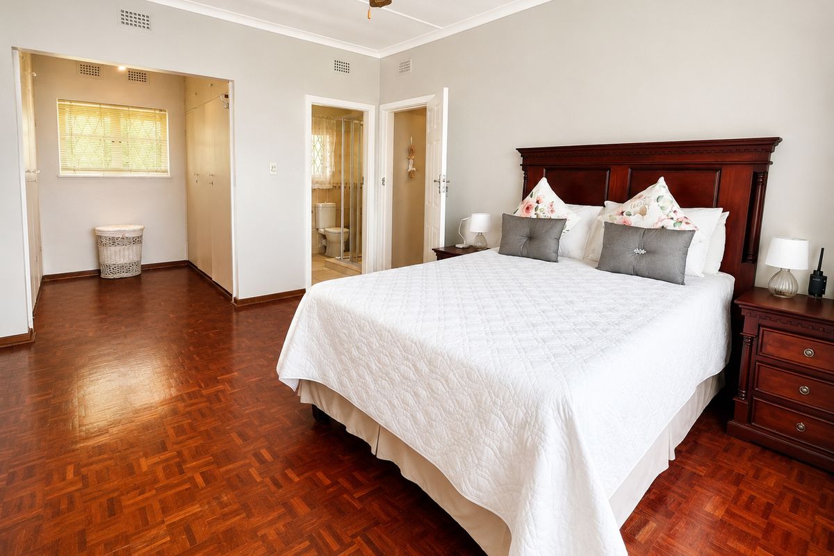Spacious bedroom featuring warm parquet flooring, built-in cupboards, and direct access to an en-suite bathroom.