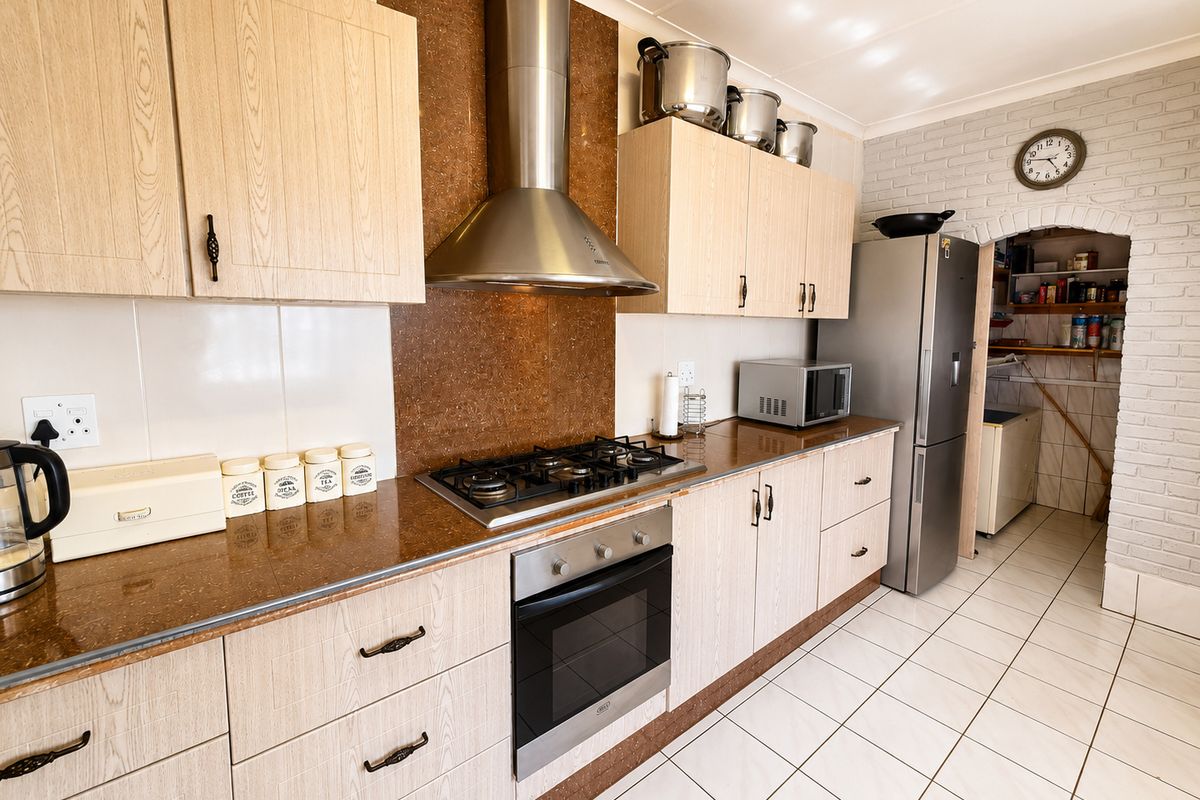 A functional kitchen featuring light wood cabinetry, stone countertops, a gas hob with extractor fan, and an adjacent scullery area with tiled flooring.