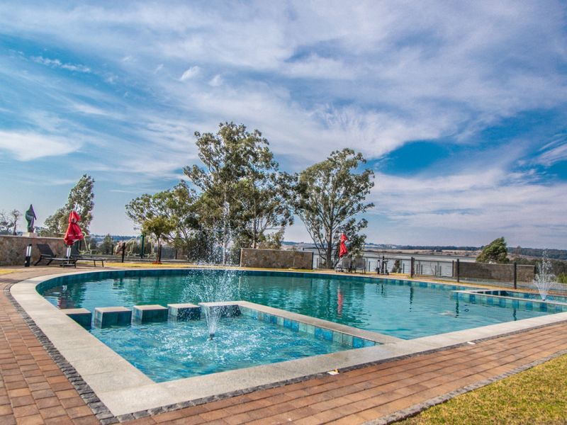 A well-maintained outdoor swimming pool area featuring a built-in water fountain, stone retaining walls, and paved decking with scenic landscape views.