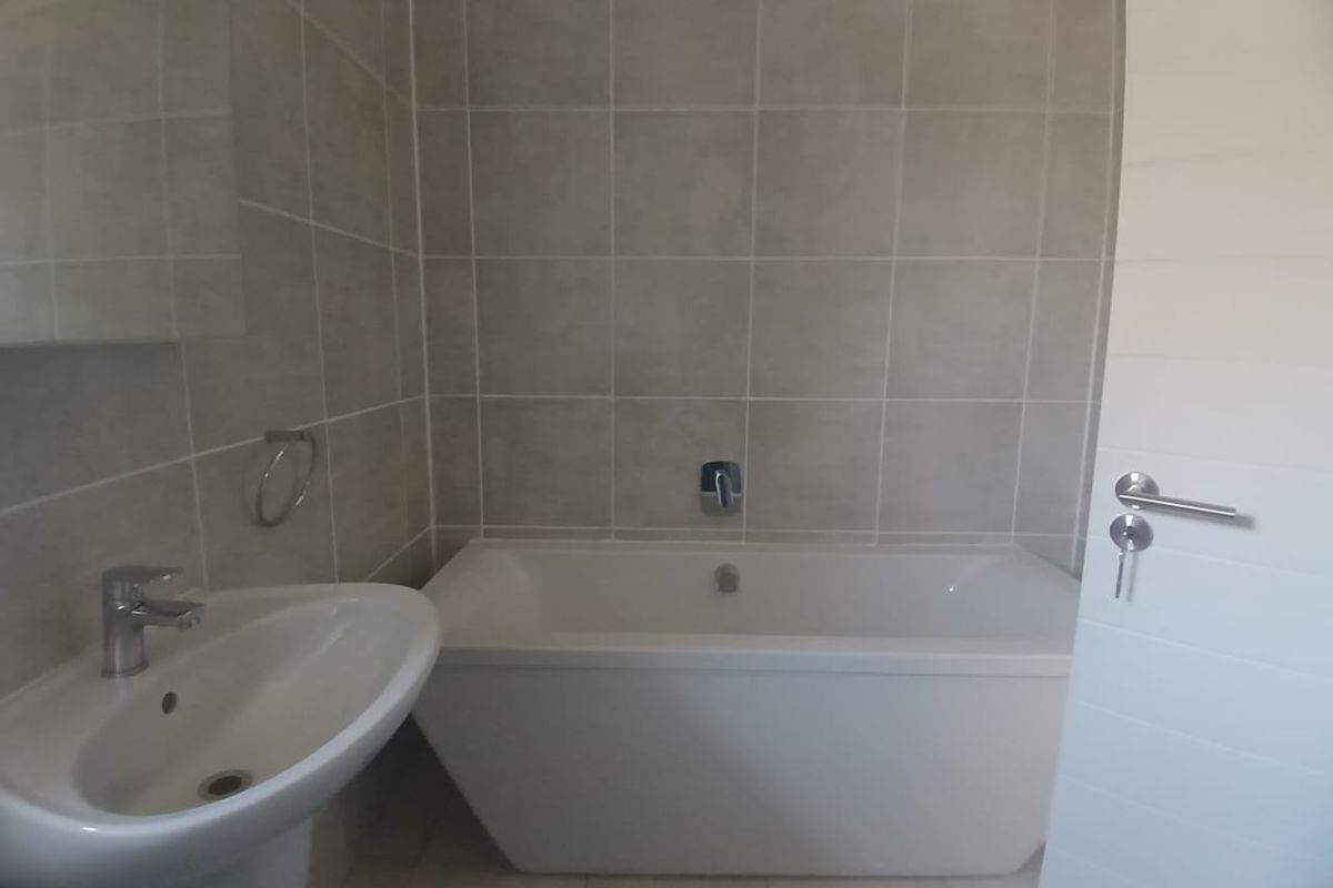 A clean, modern bathroom featuring a white pedestal basin, a built-in bathtub with chrome fixtures, and neutral wall tiling.