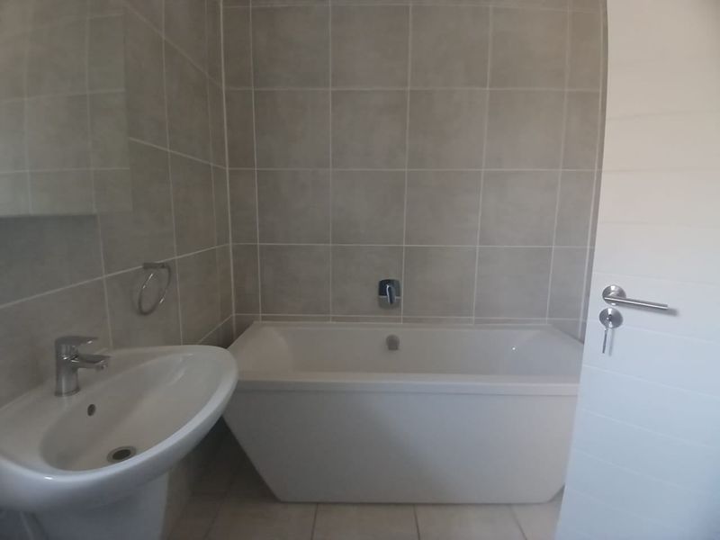 A clean, modern bathroom featuring a white pedestal basin, a built-in bathtub with chrome fixtures, and neutral wall tiling.