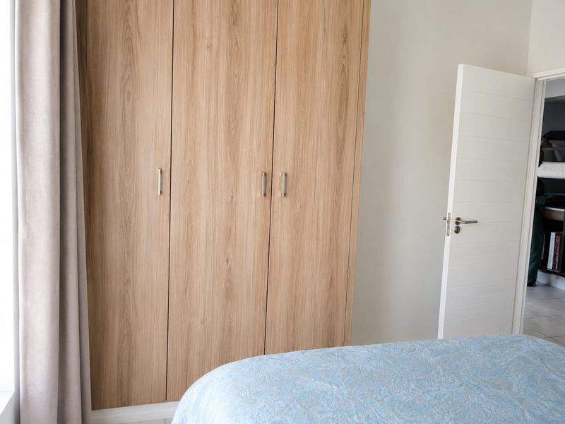 A bedroom featuring light wood-grain built-in wardrobes and a modern white internal door, offering clean lines and functional storage space.