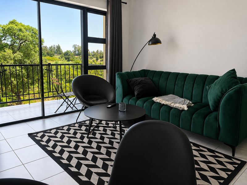 A bright living room featuring large sliding glass doors that open onto a balcony with scenic green views and tiled flooring throughout.