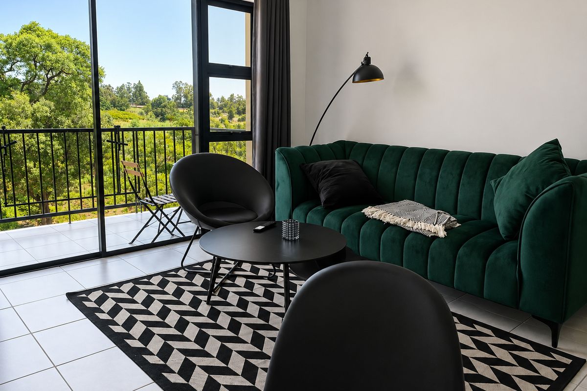 A bright living room featuring large sliding glass doors that open onto a balcony with scenic green views and tiled flooring throughout.