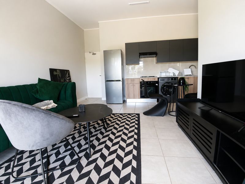 Modern open-plan living area featuring a compact kitchen with built-in cabinetry, oven, and extractor fan, seamlessly integrated with the lounge space.