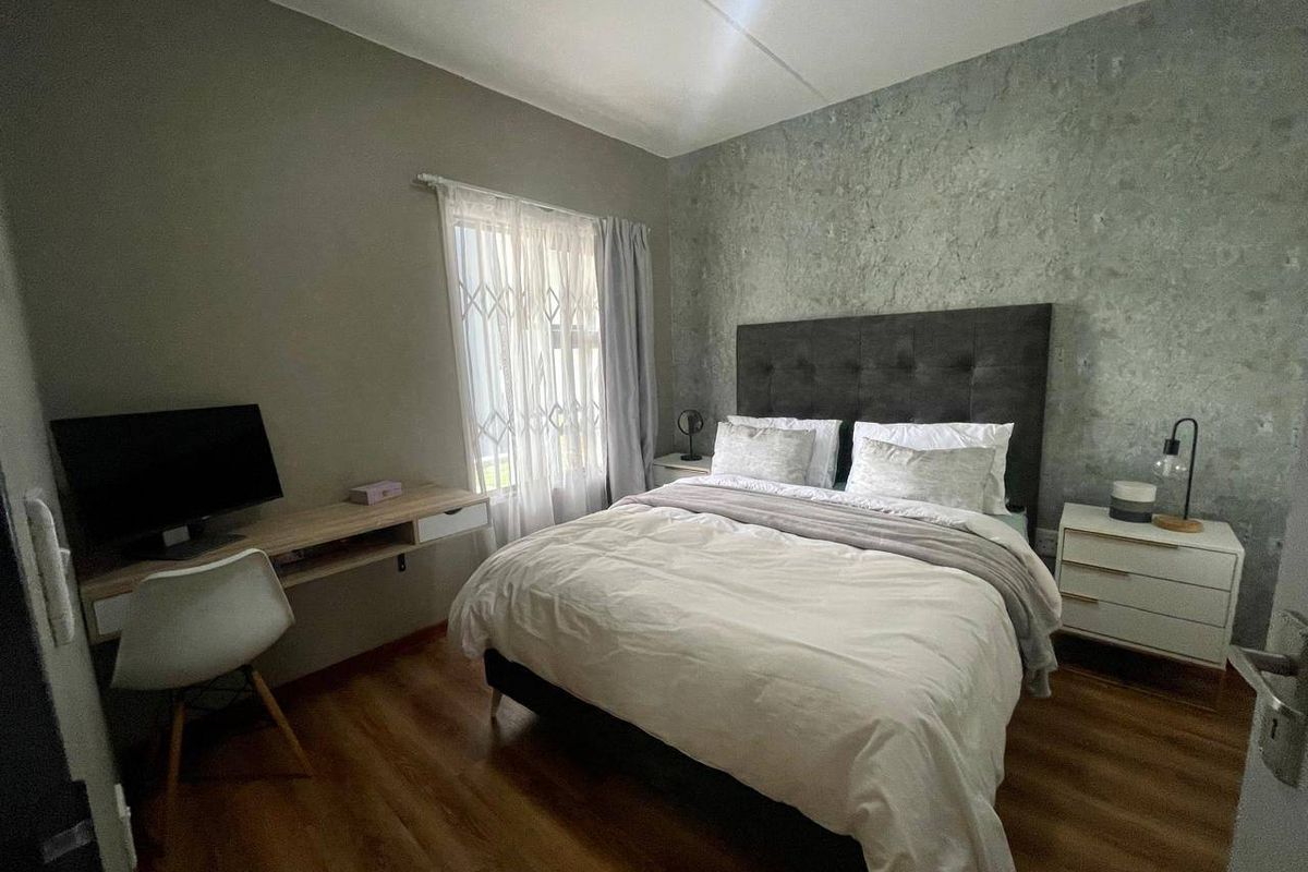 A well-maintained bedroom featuring laminate flooring, a textured feature wall, and a window fitted with a security gate.