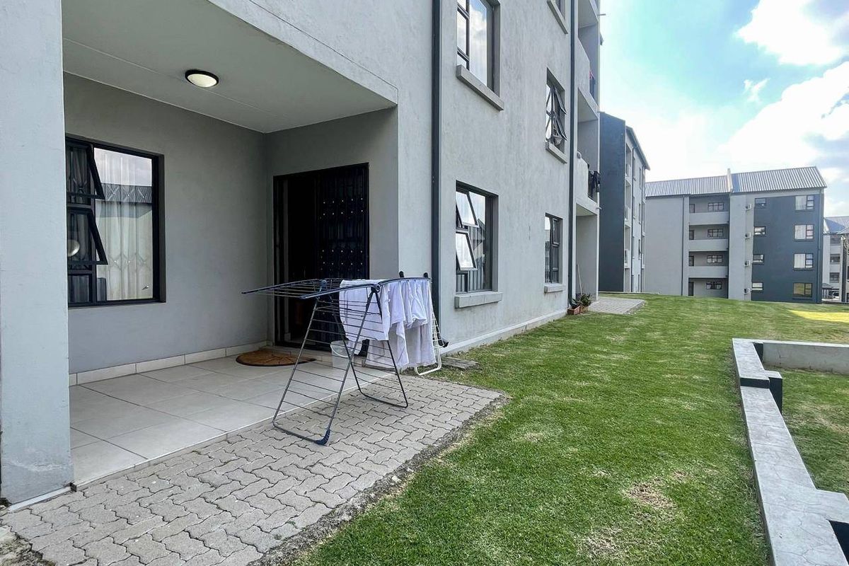 Ground floor apartment exterior featuring a paved patio area leading onto a well-maintained communal lawn and garden space.