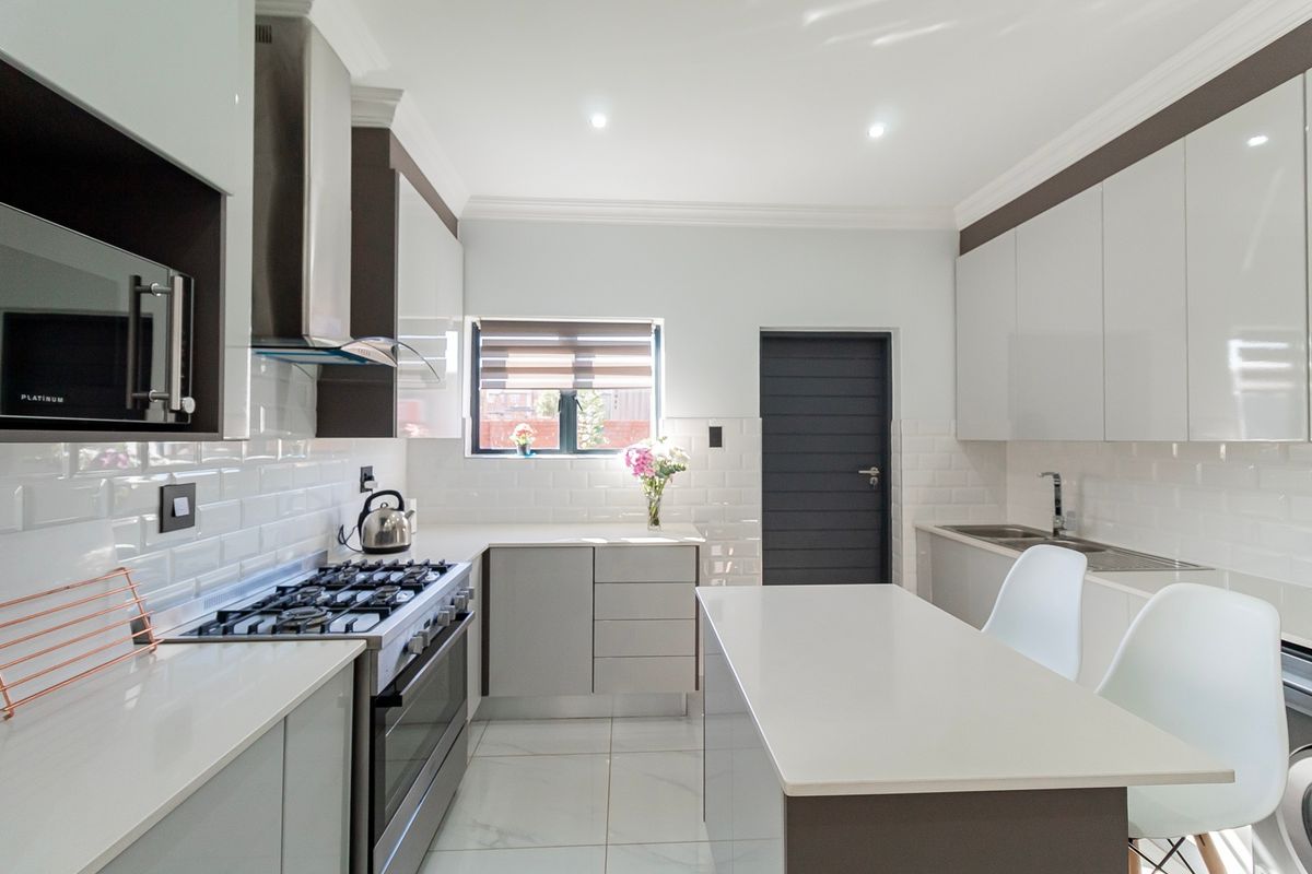 Modern kitchen featuring high-gloss cabinetry, quartz countertops, subway tile backsplash, gas hob, built-in oven, and a central island with integrated sink.
