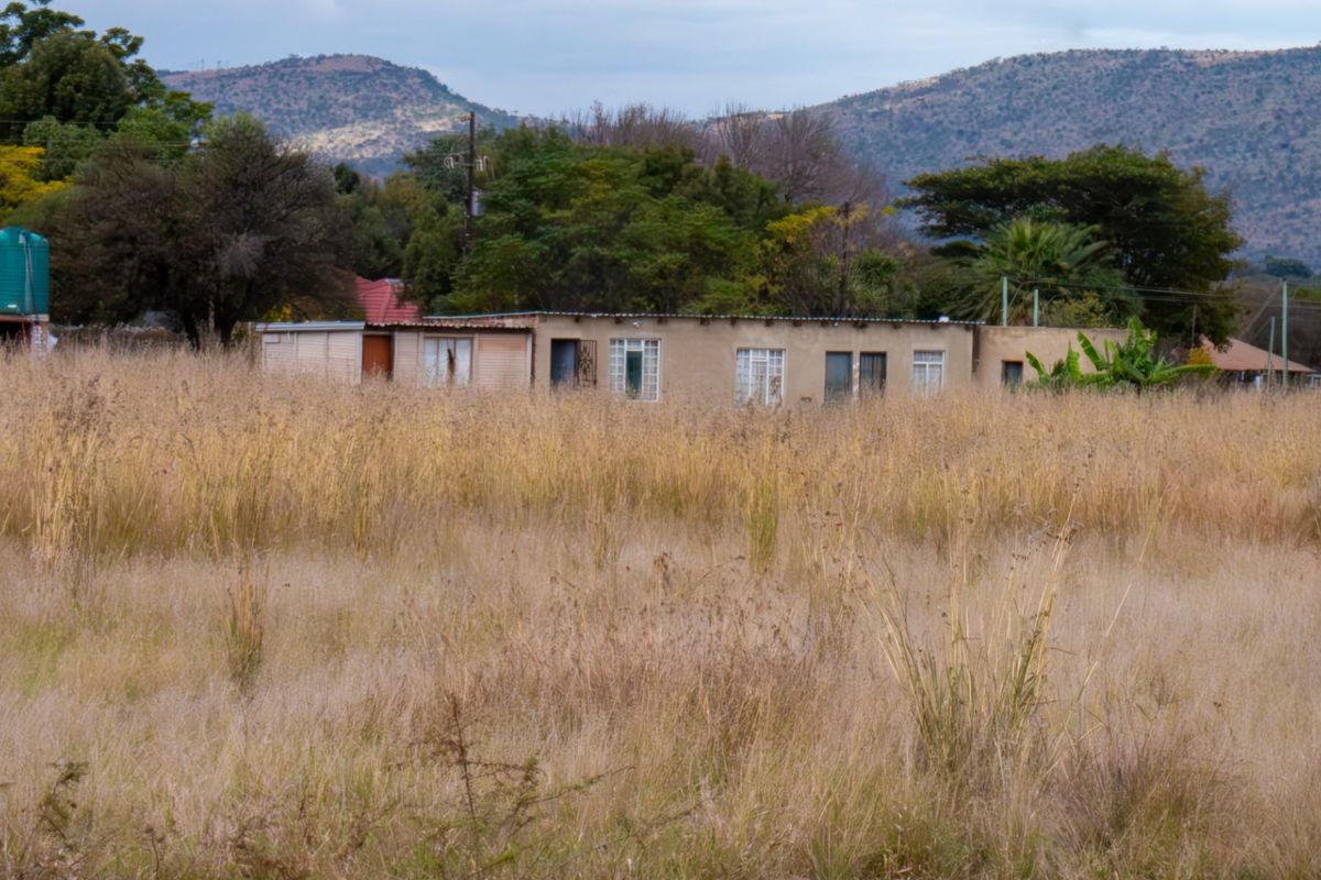 A view of the rear elevation of a farm dwelling set within a large, overgrown field with mountain views in the background.