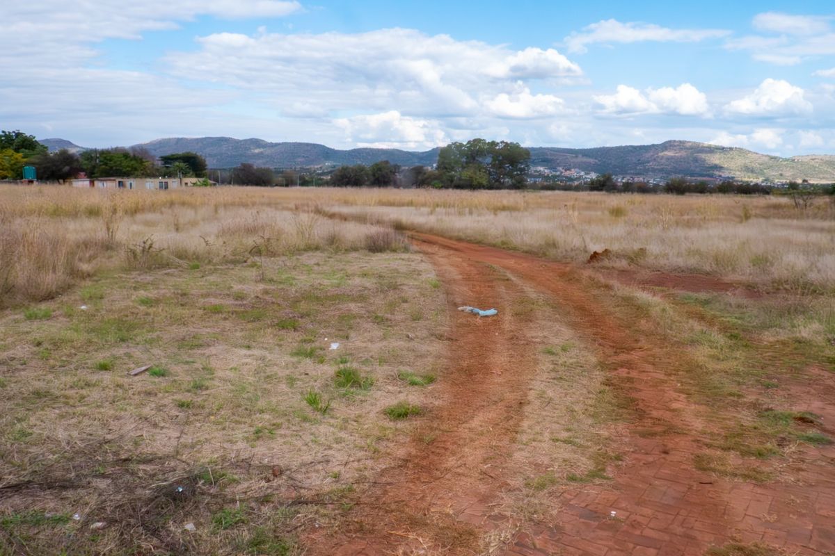 Expansive open grassland view featuring a dirt track leading through the property with distant mountain scenery.