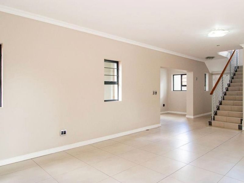 Spacious, open-plan living area featuring neutral tiled flooring, clean wall finishes, and a modern staircase with a metal balustrade.