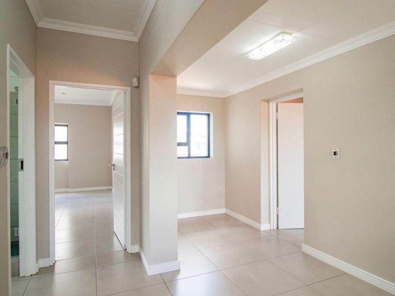 A bright, neutral-toned hallway featuring tiled flooring, coving, and multiple internal doorways leading to adjacent rooms.
