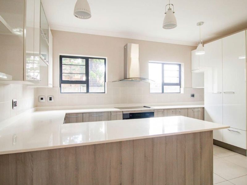 Modern kitchen featuring sleek gloss cabinetry, quartz countertops, built-in oven, electric hob, and stainless steel extractor fan with neutral tiled flooring.