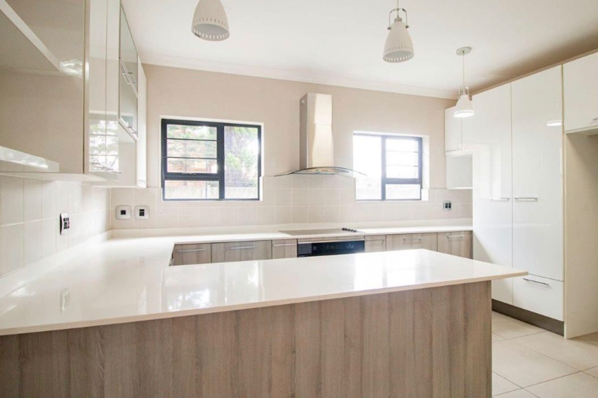 Modern kitchen featuring sleek gloss cabinetry, quartz countertops, built-in oven, electric hob, and stainless steel extractor fan with neutral tiled flooring.