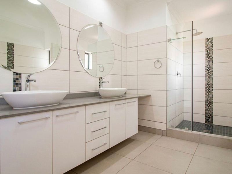 Modern bathroom featuring a double vanity with vessel sinks, large wall mirrors, and a spacious walk-in shower with glass enclosure and mosaic tile accents.