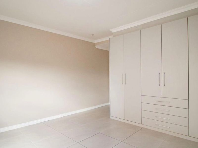 A bright, empty bedroom featuring neutral walls, tiled flooring, and extensive built-in cupboards with integrated drawer storage.