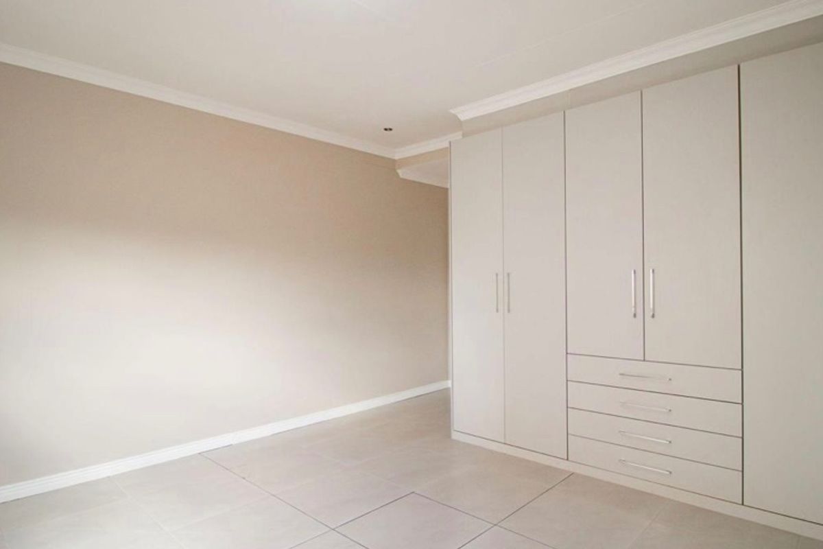 A bright, empty bedroom featuring neutral walls, tiled flooring, and extensive built-in cupboards with integrated drawer storage.