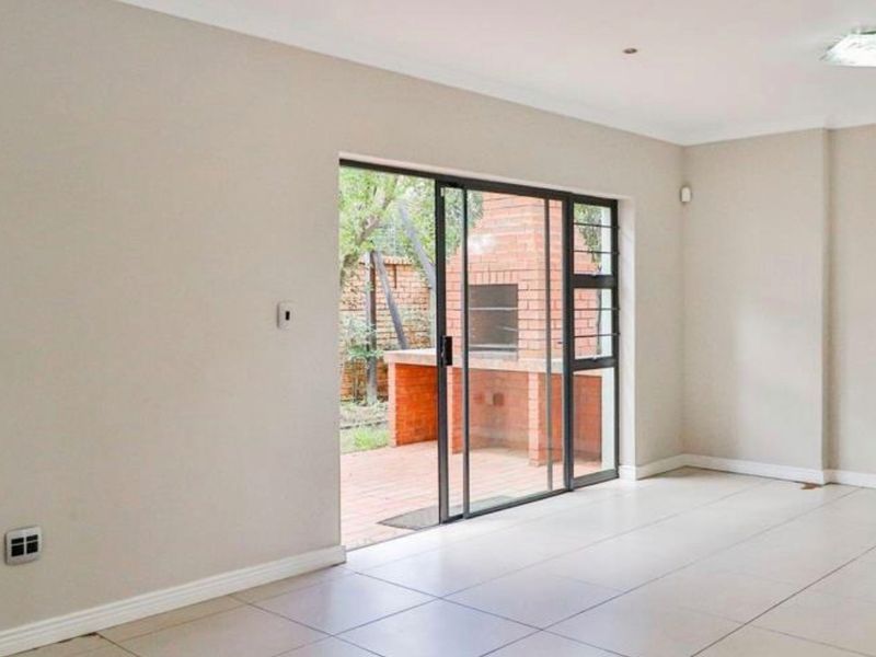 Bright, empty living room featuring large sliding glass doors that open onto a patio with a built-in brick braai.