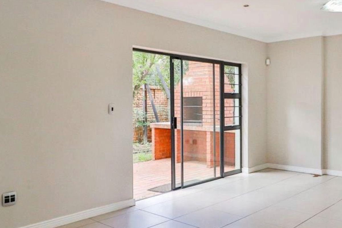 Bright, empty living room featuring large sliding glass doors that open onto a patio with a built-in brick braai.