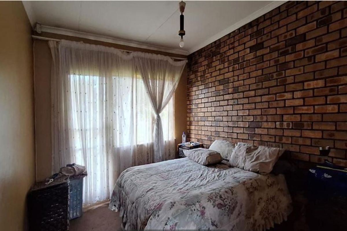 A bedroom featuring an exposed brick feature wall and large window with curtain tracks, offering a dated aesthetic ready for modernization.