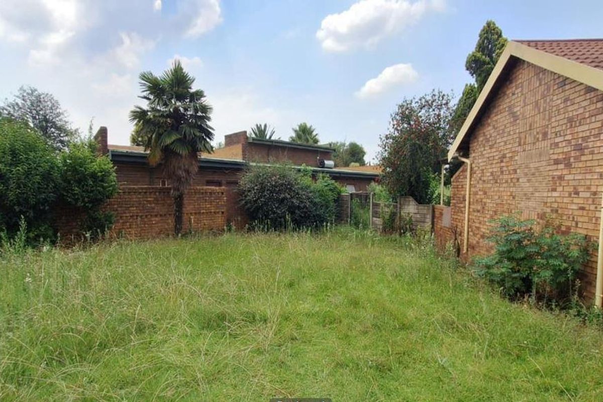 A rear view of the property featuring a brick exterior and an expansive, unmaintained garden area with a perimeter brick boundary wall.