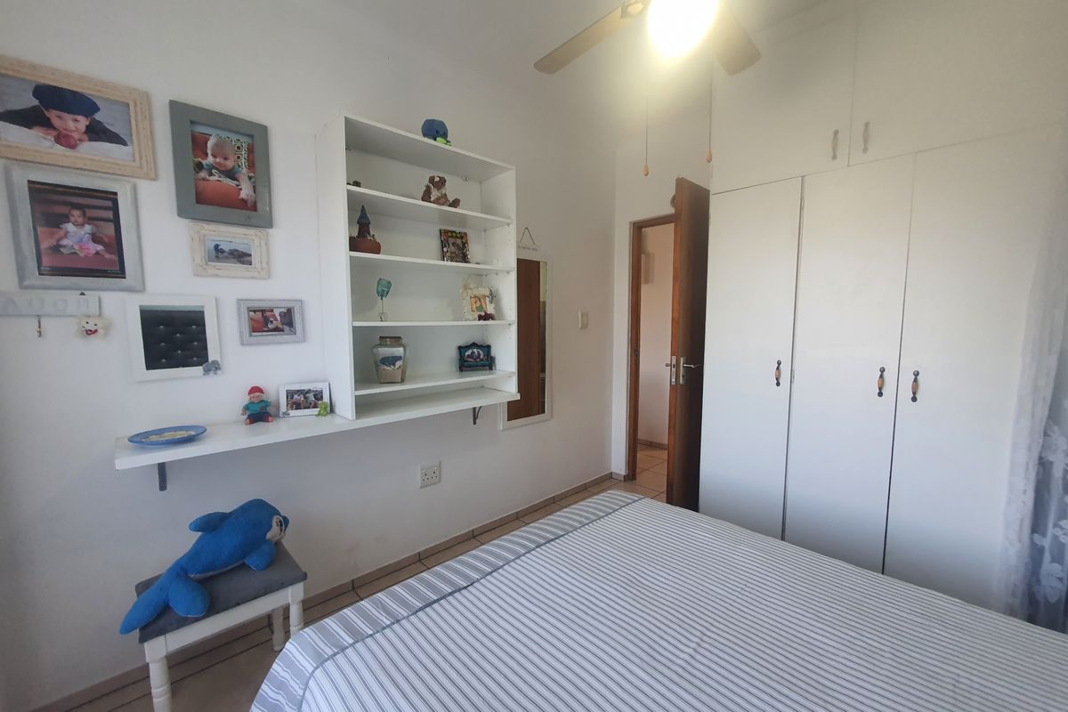 A functional bedroom featuring built-in cupboards, a ceiling fan, and wall-mounted shelving, providing practical storage and climate control.