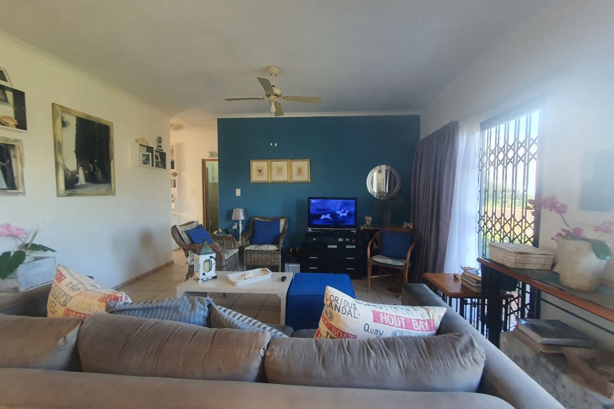 A comfortable living room featuring tiled flooring, a ceiling fan, and a security gate leading to the exterior.
