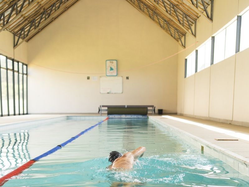 An indoor swimming pool facility featuring high ceilings with exposed timber trusses and large windows providing ample natural light.