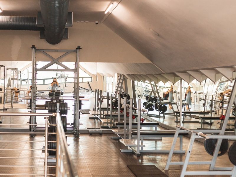 A well-equipped gym featuring mirrored walls, exposed industrial ductwork, and durable flooring, providing a functional space for fitness activities.