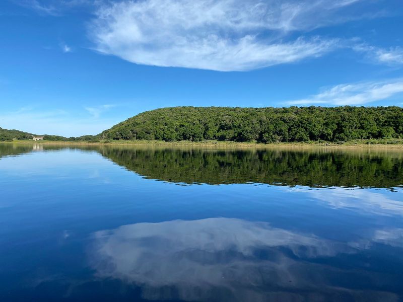 A scenic view of a calm lake reflecting the blue sky and surrounding lush green hillside.