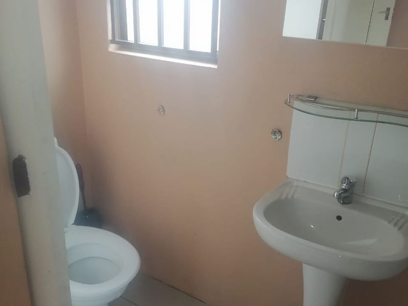 A functional bathroom featuring a pedestal basin, toilet, and tiled flooring, with a window fitted with security bars.