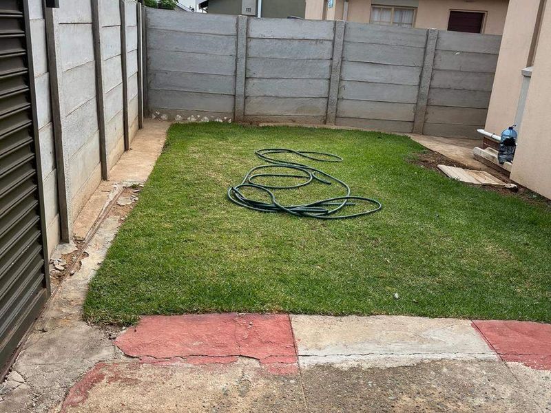 A rear garden area featuring a small lawn, enclosed by precast concrete boundary walls, with weathered concrete paving requiring maintenance or resurfacing.