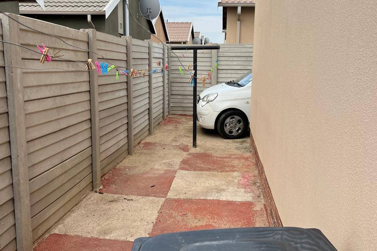 A narrow side yard area featuring a precast concrete boundary wall and painted concrete paving, currently used as a utility space.